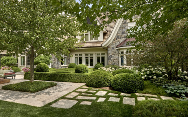 View featuring a formal garden with box hedges and rounded shrub accents complementing the curvilinear design of the adjacent yards, enhanced by a stone stepper path with grass joints leading out of the space
